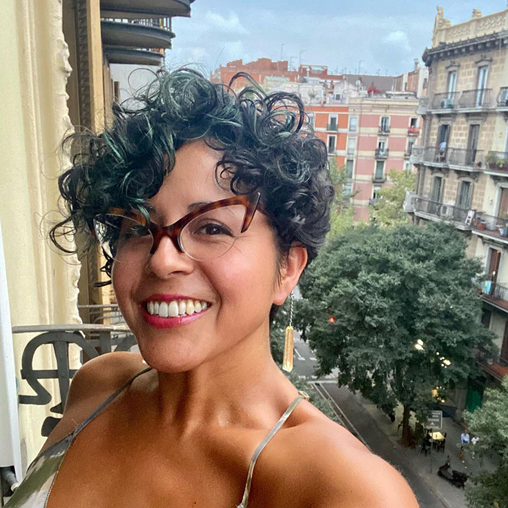 Favianna is wearing glasses and smiling while on a balcony in Barcelona.